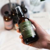 Model's hand holding and about to use Bergamot Coconut & Sesame Hair Mask Oil with one hand.