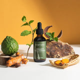 A bottle of SUDTANA's Bergamot Mint & Turmeric Scalp Revival Treatment with peppermint leaves, sliced turmeric, and bergamot for a soothing scalp oil treatment.