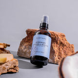 SUDTANA Rosemary Ginger & Sesame Uplifting Body Oil bottle (120ml), a Thai herbal body oil for deep hydration and glowing skin, -placed on natural stones with fresh ginger slices.