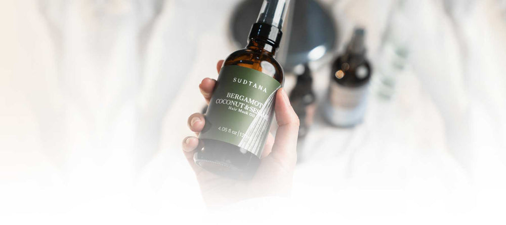 Model’s hand holding and about to use Bergamot Coconut & Sesame Hair Mask Oil with one hand.