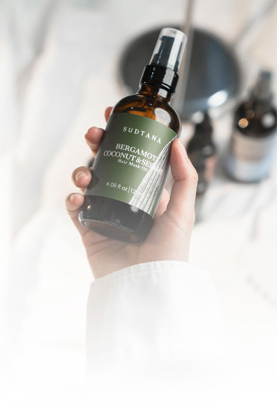 Model’s hand holding and about to use Bergamot Coconut & Sesame Hair Mask Oil with one hand.
