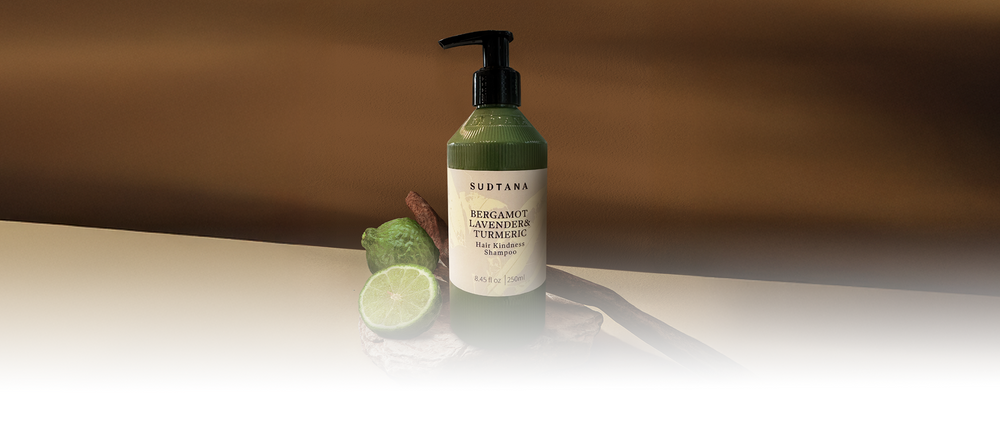 SUDTANA’s Hair Kindness Shampoo with Bergamot, Lavender & Turmeric, featured with halved bergamot on natural stone.