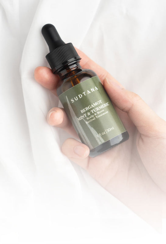 Model’s hand holding and about to use Bergamot Mint & Turmeric Scalp Revival Treatment, an all-natural dry scalp treatment designed to nourish and strengthen your hair from roots to ends.