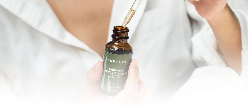 Close-up of a person applying SUDTANA’s Bergamot Mint & Turmeric Scalp Revival Treatment with a dropper, showing the product's clear, lightweight consistency. 