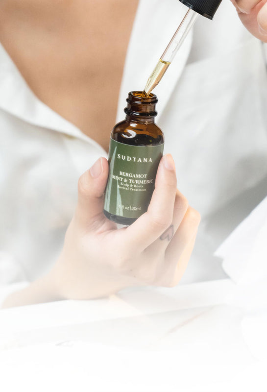Close-up of a person applying SUDTANA’s Bergamot Mint & Turmeric Scalp Revival Treatment with a dropper, showing the product's clear, lightweight consistency. 