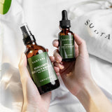 Model holding bottles of SUDTANA’s Bergamot Coconut & Sesame Hair Mask Oil and Bergamot Mint & Turmeric Scalp Revival Treatment, the award-winning duo perfect for damaged hair and irritated scalp.