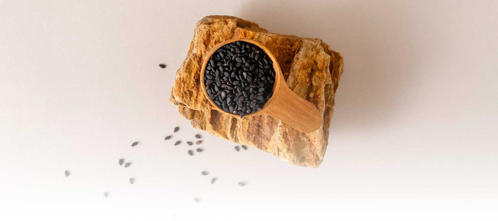 Organic black sesame seeds sustainably sourced from Thailand, displayed in a wooden scoop on natural stone and showcasing Sudtana’s commitment to clean, eco-friendly ingredients.