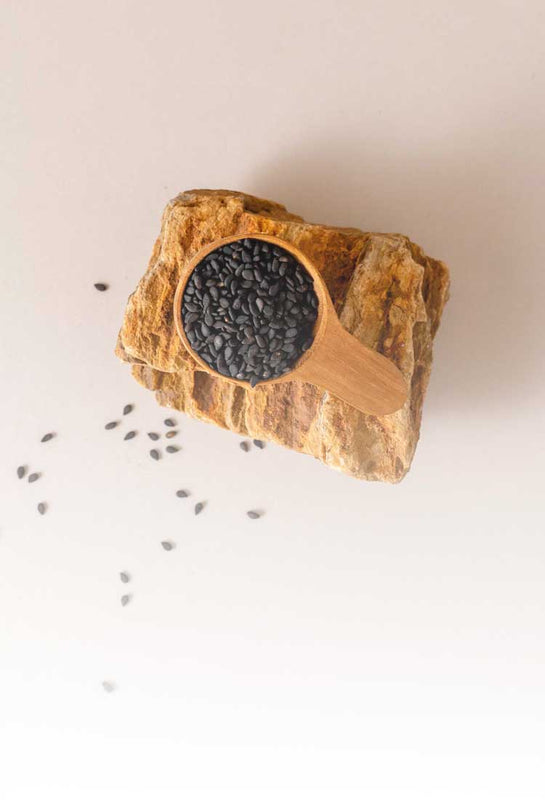 Organic black sesame seeds sustainably sourced from Thailand, displayed in a wooden scoop on natural stone and showcasing Sudtana’s commitment to clean, eco-friendly ingredients.