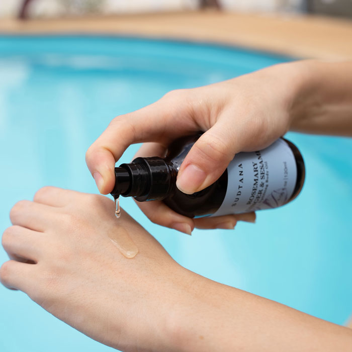 Model’s hand holding and pumping out a few drops of the Rosemary Ginger and Sesame Uplifting Body Oil, revealing its clear, lightweight texture.