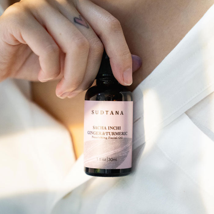A neat and clean lifestyle photo of a model holding the SUDTANA Sacha Inchi Ginger & Turmeric Facial Oil, a must-have for radiant, youthful glow.